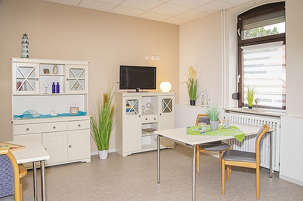 Aufenthaltsraum mit Fenster, TV-Schrank, Tischen und Sitzgelegenheiten