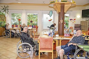 Bewohner im Rollstuhl sitzend an den Tischen des Aufenthaltsraums